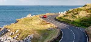 a vehicle driving on a road with the sea to the left hand side.