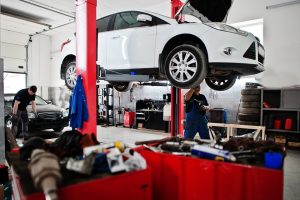 A car on a two post workshop lift in a garage with a mechanic providing a vehicle service